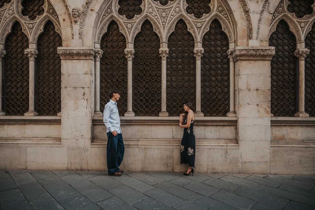 A Lucca anniversary photoshoot beneath Gothic arches Wide photograph of Alice and Pablo holding hands beneath a row of carved Gothic arches. From Alice and Pablo’s Lucca anniversary photoshoot.