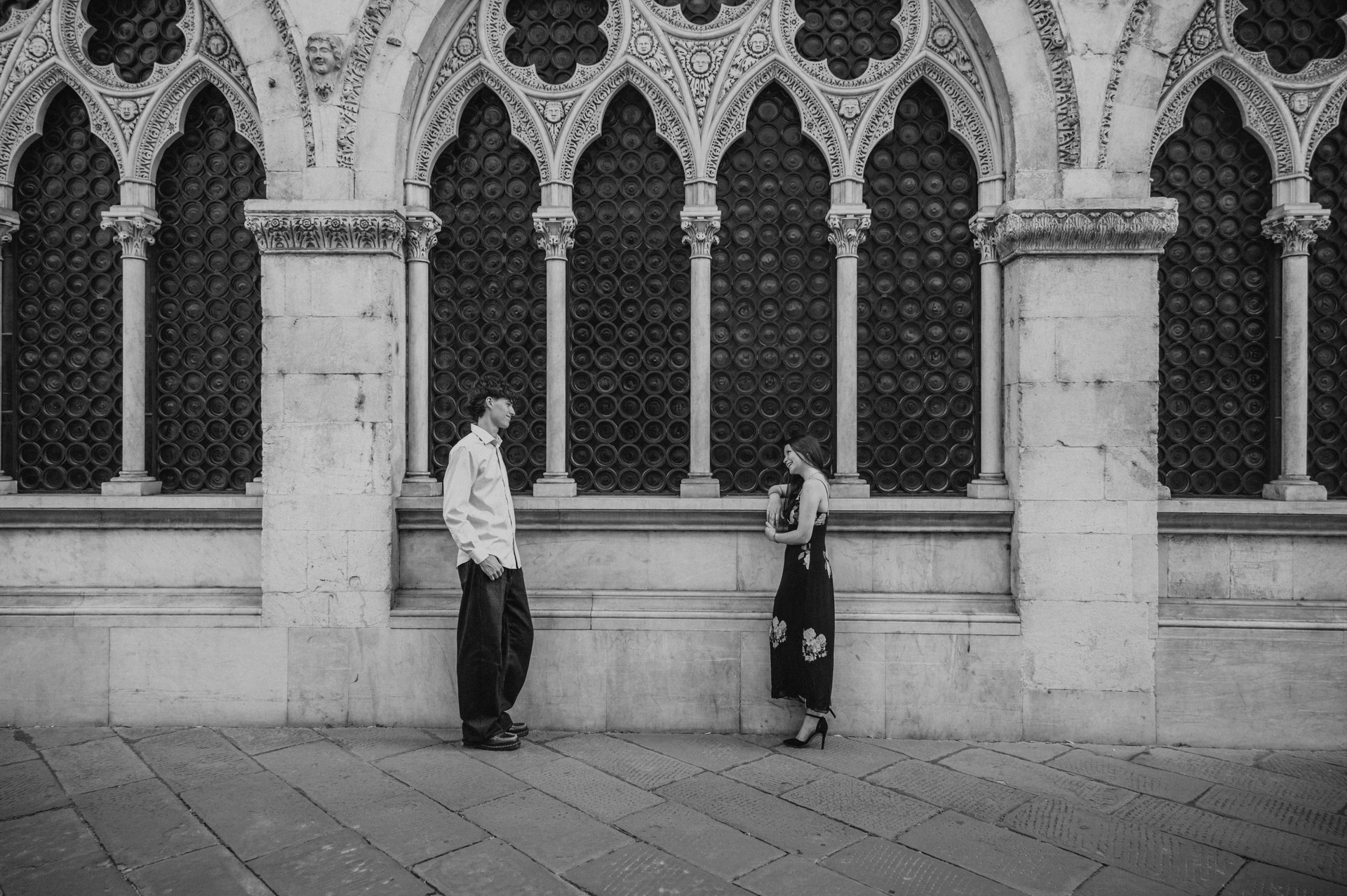 Black-and-white view of Alice and Pablo holding hands against the old town’s carved stone arches. From Alice and Pablo’s Lucca anniversary photoshoot.