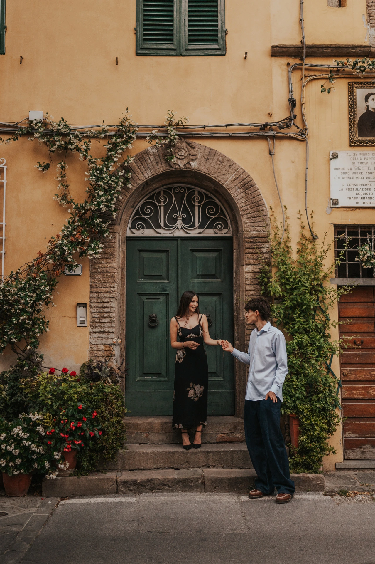 Alice and Pablo hold hands outside a green doorway framed by climbing flowers and warm ochre walls. From Alice and Pablo’s Lucca anniversary photoshoot.