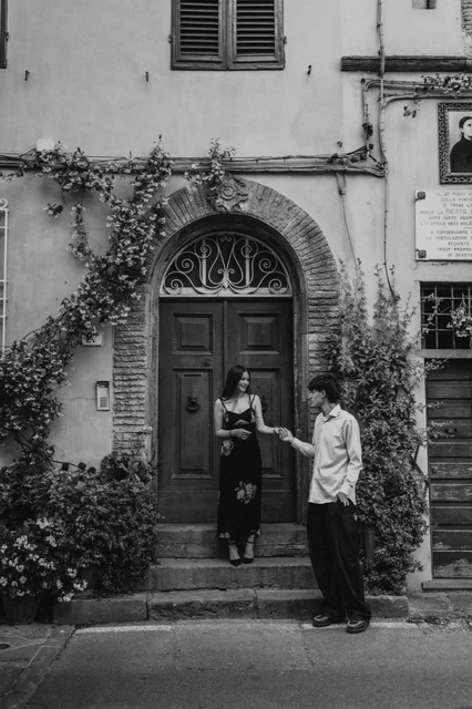 Lucca couple photoshoot at a flower-framed doorway, in black and white Black-and-white portrait of Alice and Pablo outside an old-town doorway framed by climbing plants. From Alice and Pablo’s Lucca anniversary photoshoot.