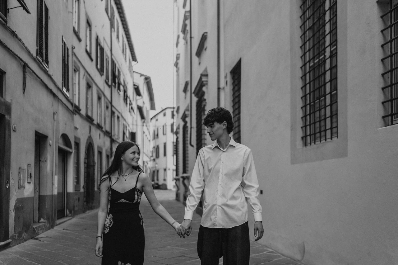 A black-and-white old-town walk during a Lucca couple photoshoot Black-and-white photograph of Alice and Pablo walking hand in hand through Lucca’s narrow streets. From Alice and Pablo’s Lucca anniversary photoshoot.