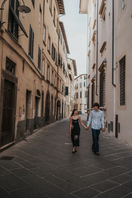 Lucca couple photoshoot along a stone-paved old-town street Alice and Pablo walk towards the camera through a long stone-paved lane in Lucca’s old town. From Alice and Pablo’s Lucca anniversary photoshoot.