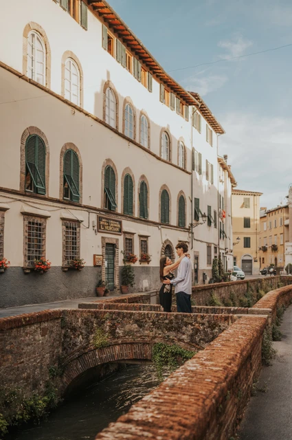 Via del Fosso canal setting for a Lucca photoshoot Lucca’s narrow canal passes beneath a brick bridge beside white buildings with green shutters. From Alice and Pablo’s Lucca anniversary photoshoot.