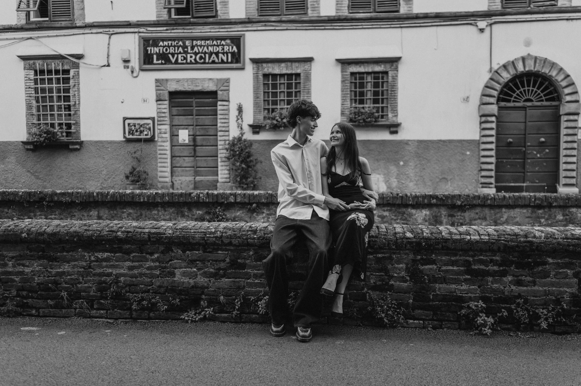 Black-and-white photograph of Alice and Pablo sharing a close moment by a brick parapet on Via del Fosso. From Alice and Pablo’s Lucca anniversary photoshoot.