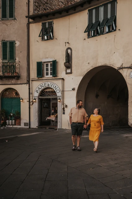 Lucca couple photoshoot: an arched entrance to Piazza dell’Anfiteatro The couple walking together beneath the tall buildings beside an arched entrance to Piazza dell’Anfiteatro during a couple photoshoot in Lucca.