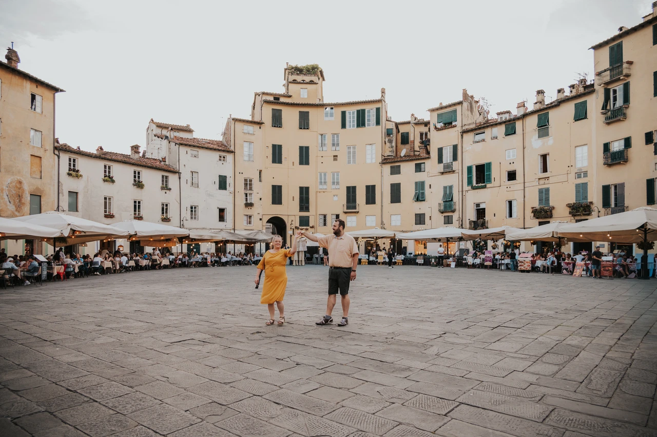 Lucca couple photoshoot: walking across the open piazza A wide view of the couple walking away across the open paving of Piazza dell’Anfiteatro during a couple photoshoot in Lucca.