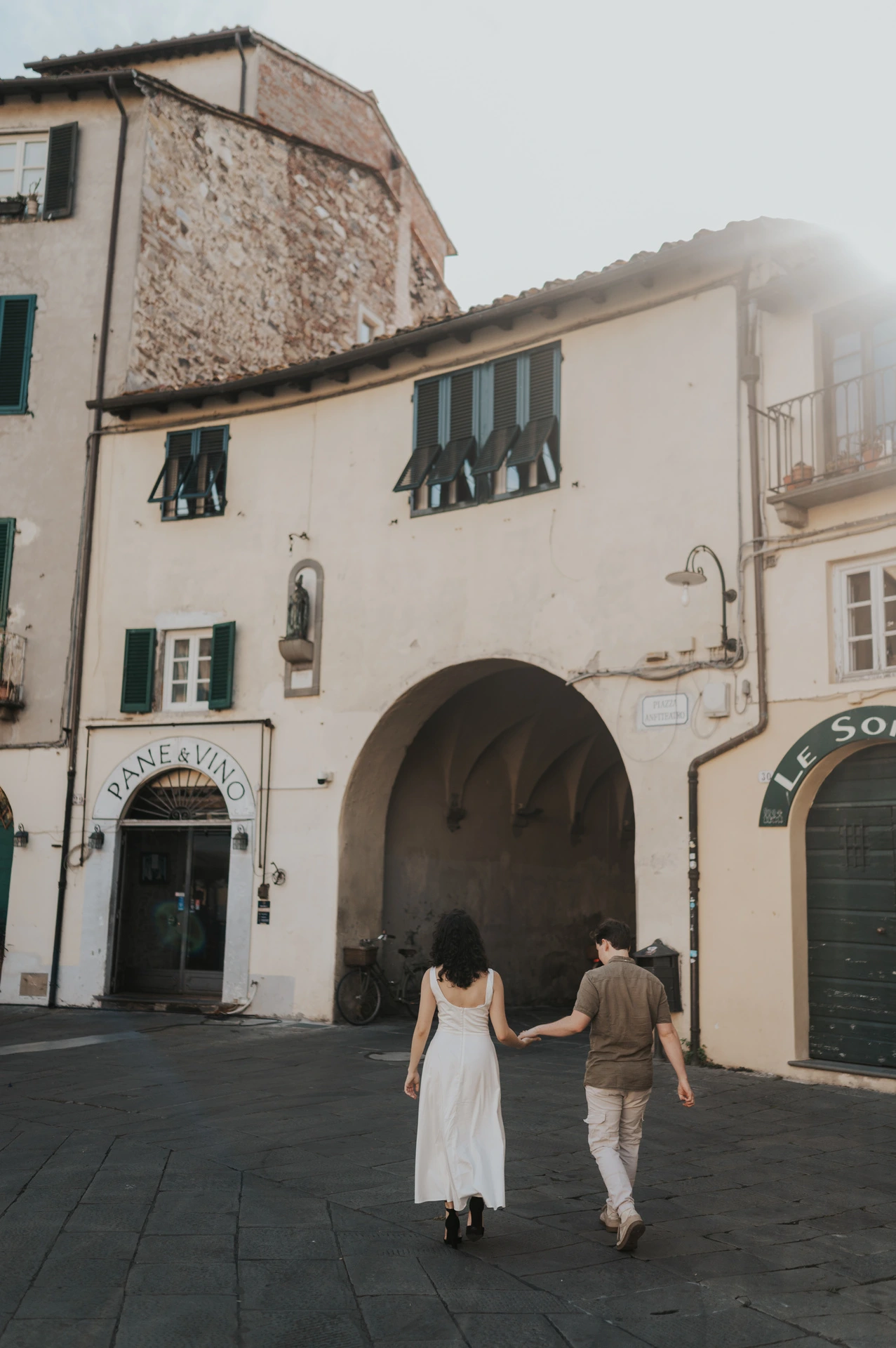 The couple walking away towards an arched entrance in Piazza dell’Anfiteatro during a couple photoshoot in Lucca.