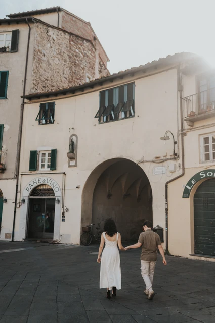 Lucca couple photoshoot: walking towards the piazza’s stone arch The couple walking away towards an arched entrance in Piazza dell’Anfiteatro during a couple photoshoot in Lucca.