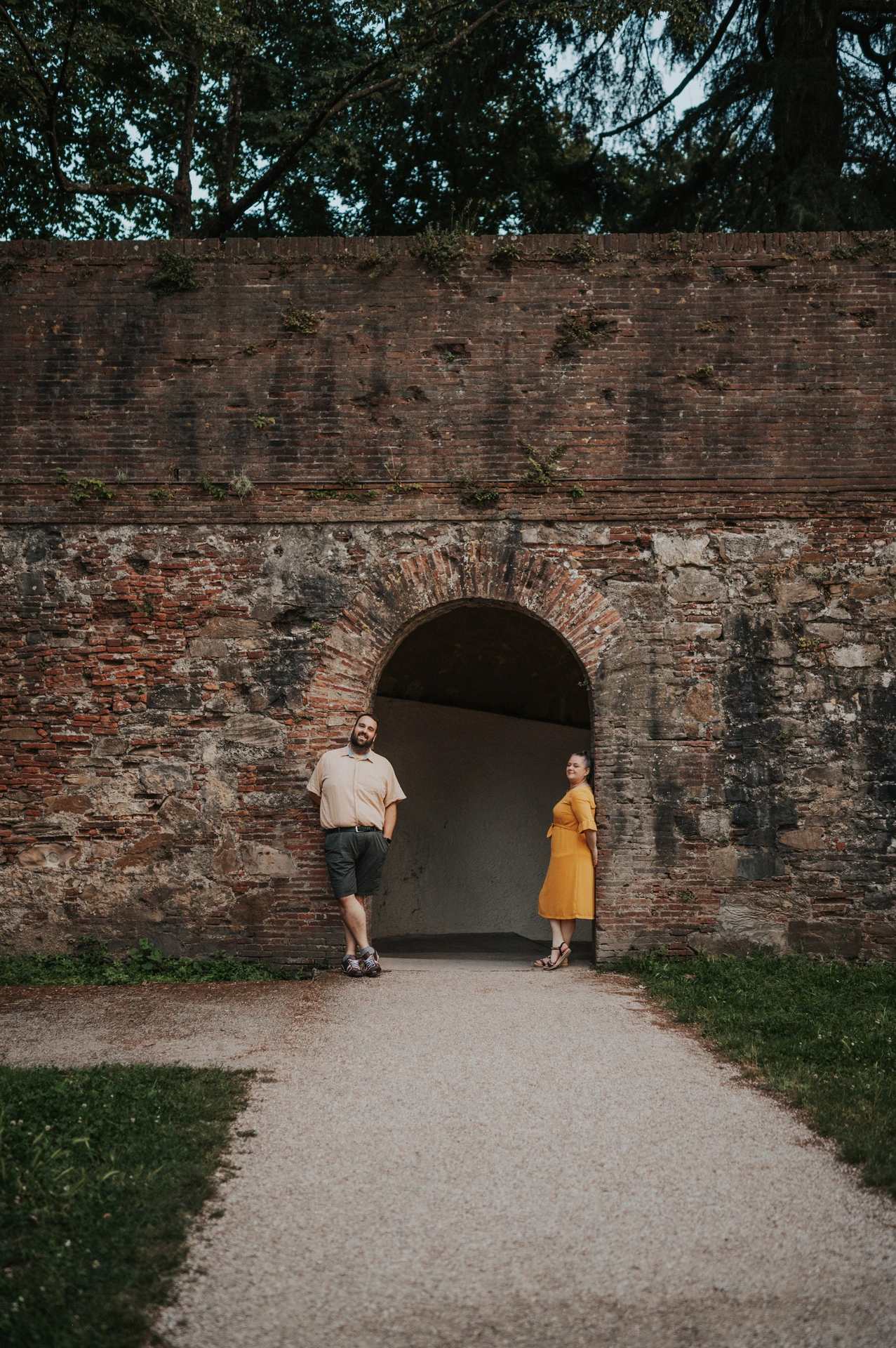 The couple standing on either side of an arched passage through Lucca’s brick city walls during a couple photoshoot in Lucca.