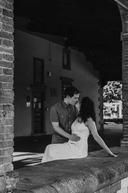 Lucca couple photoshoot: a portrait beneath a city-wall arch in black and white Black-and-white photograph of the couple leaning close beneath an arch beside the city walls during a couple photoshoot in Lucca.