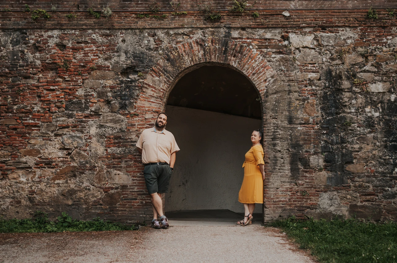 Lucca couple photoshoot: a wide portrait beside the brick arch A wide portrait of the couple standing apart beside a brick arch in Lucca’s city walls during a couple photoshoot in Lucca.