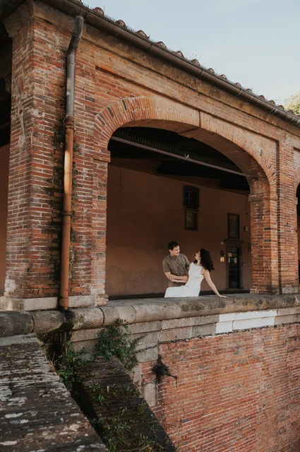Lucca couple photoshoot: a brick arch beside the city walls A wide view of the couple beside a brick arch and stone ledge at the city walls during a couple photoshoot in Lucca.
