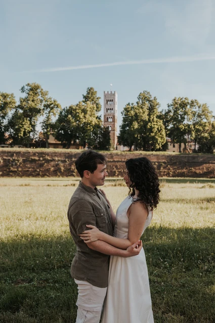 Lucca couple photoshoot: an embrace with San Frediano’s bell tower The couple embracing beside a grassy area with San Frediano’s bell tower behind them during a couple photoshoot in Lucca.