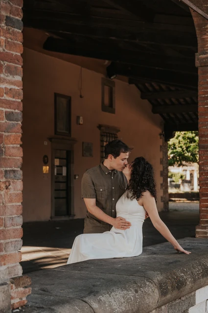 Lucca couple photoshoot: a close moment beneath the brick arch The couple leaning close beside a stone ledge beneath a brick arch at the city walls during a couple photoshoot in Lucca.