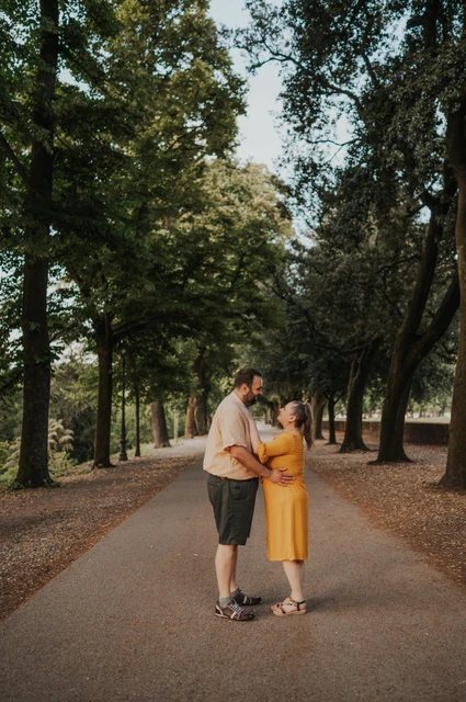 Lucca couple photoshoot: a yellow dress on a leafy path The couple standing close on a tree-lined path, with the woman’s yellow dress against the greenery during a couple photoshoot in Lucca.