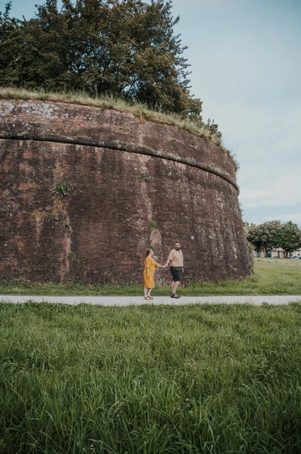 Lucca couple photoshoot: a walk beside the curved brick walls The couple walking together beside the tall curved brickwork of Lucca’s city walls during a couple photoshoot in Lucca.