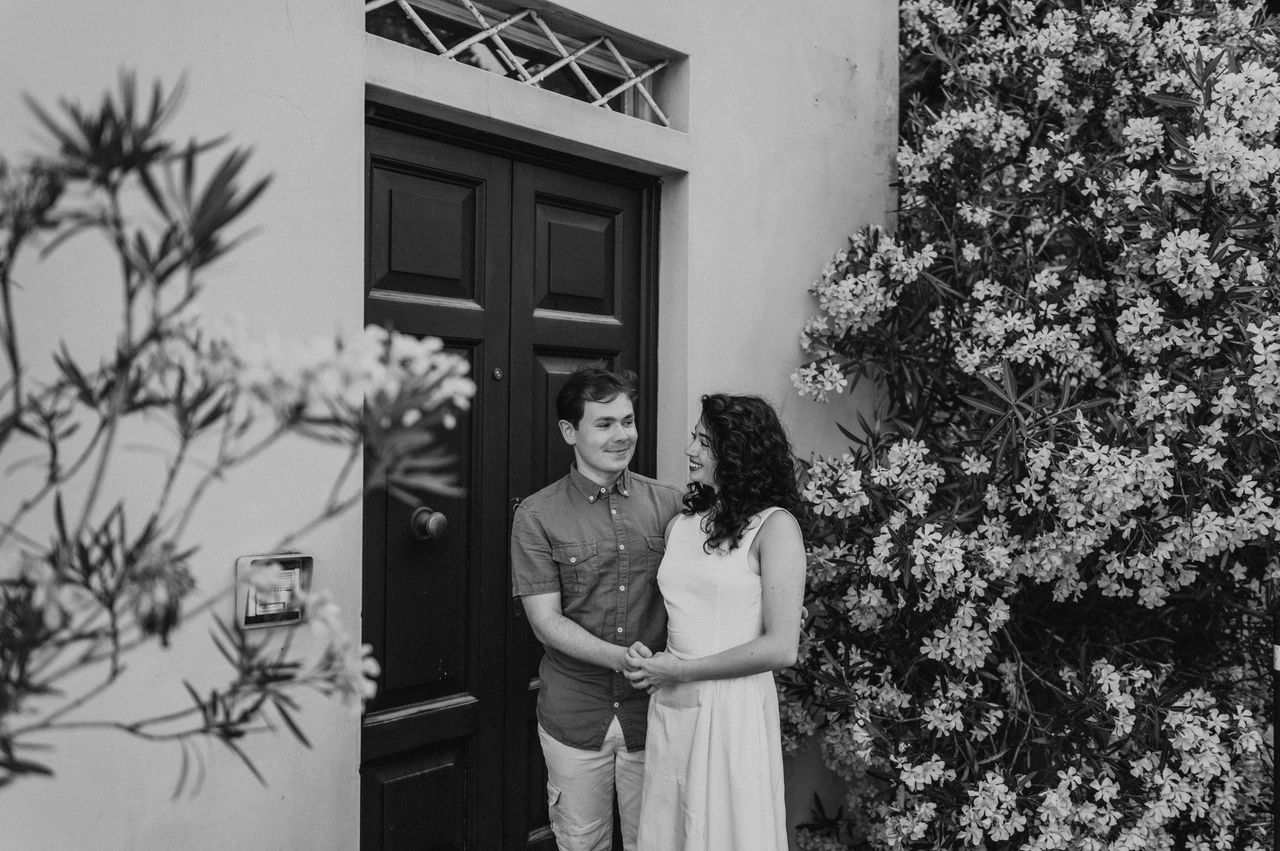 Lucca couple photoshoot: a flowering doorway in the old town in black and white Black-and-white photograph of the couple embracing beside a dark door and flowering branches in the old town during a couple photoshoot in Lucca.