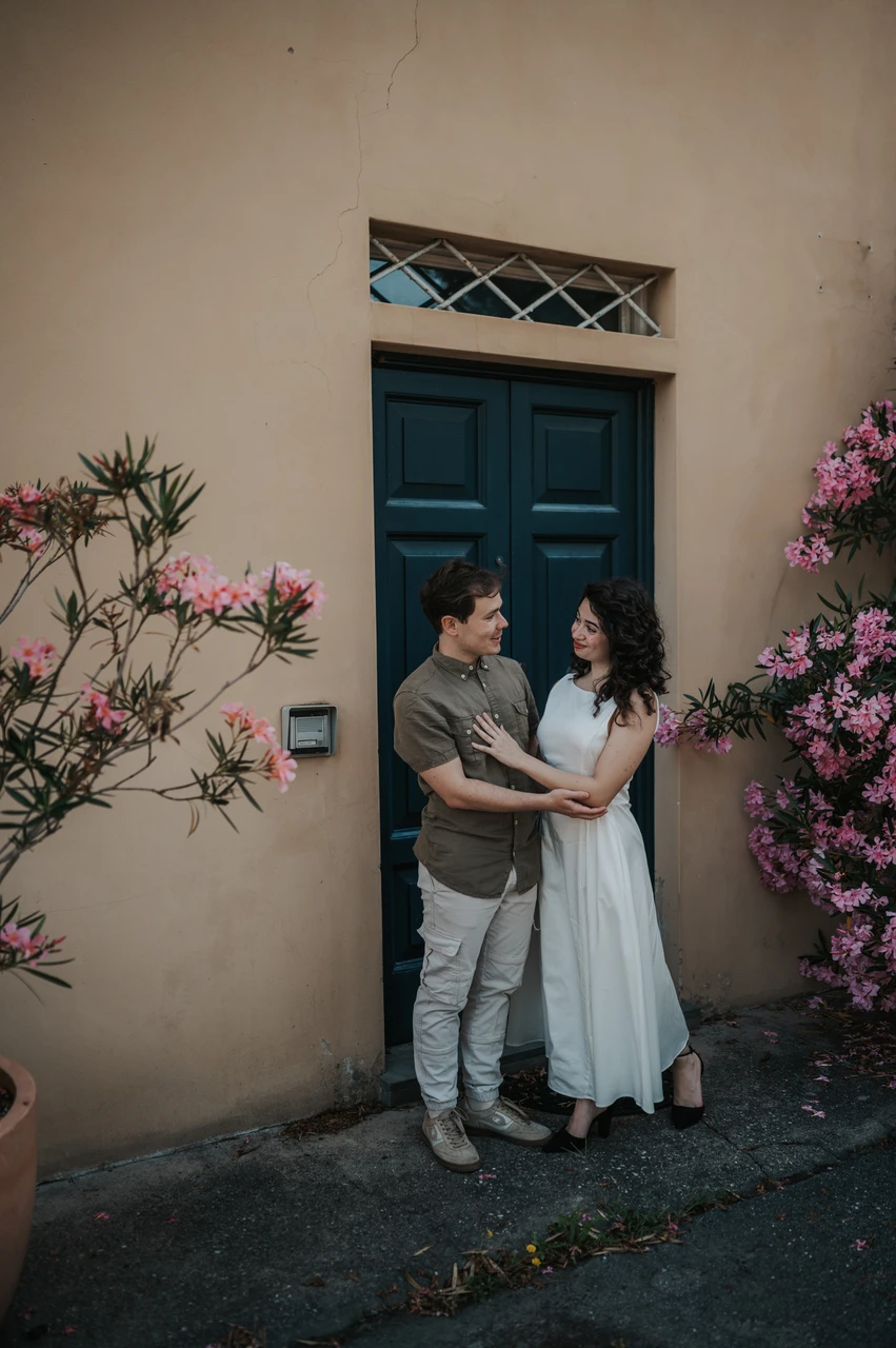Lucca couple photoshoot: a green door and pink flowers in the old town The couple embracing beside a green door and pink flowers in a narrow old-town lane during a couple photoshoot in Lucca.