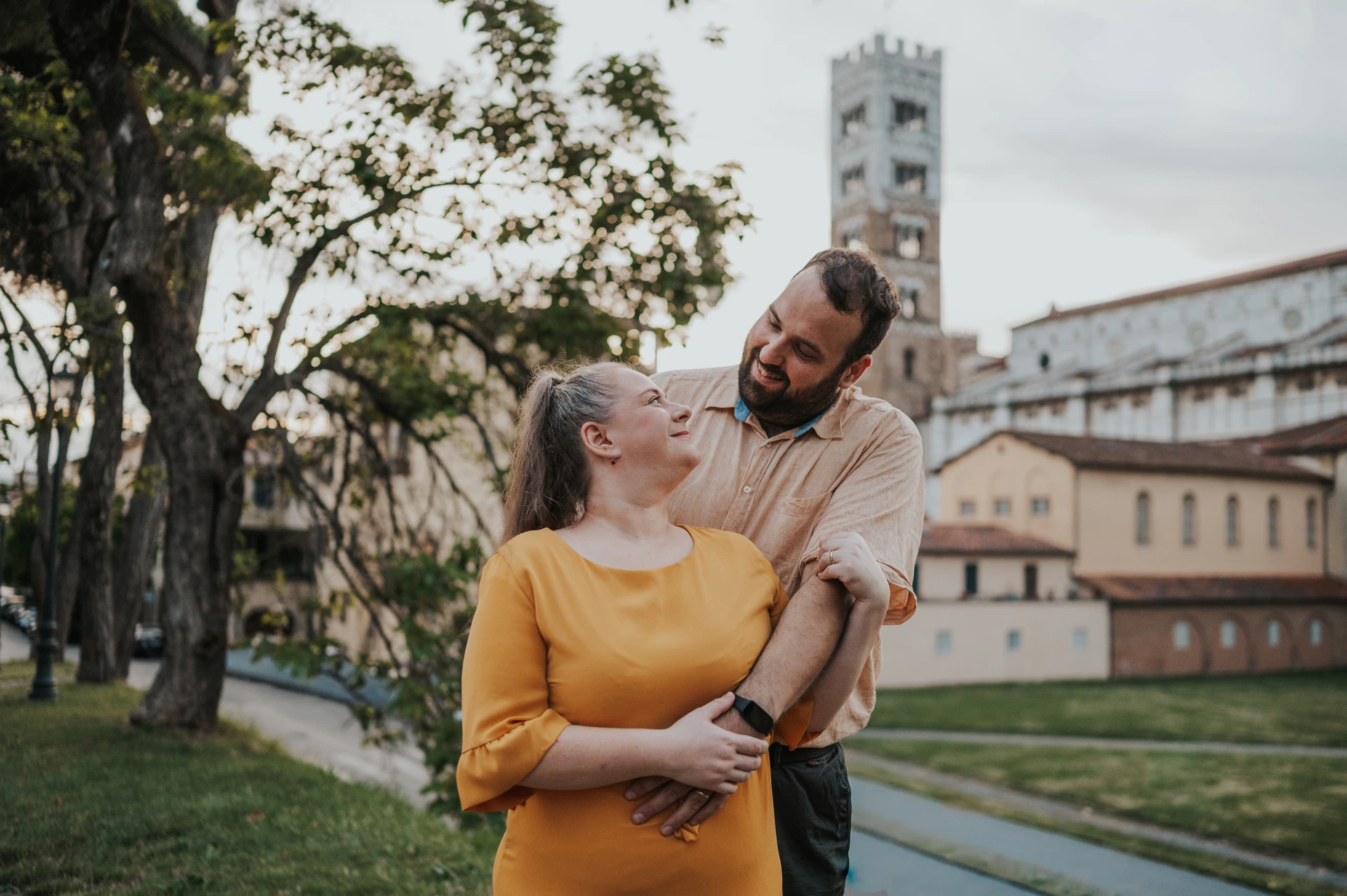 The couple laughing together with trees and San Frediano’s bell tower in the background during a couple photoshoot in Lucca.