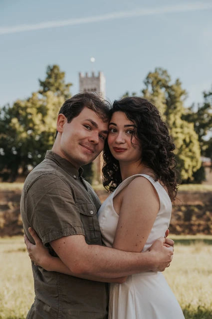 Lucca couple photoshoot: a close portrait by San Frediano’s tower A close portrait of the couple embracing with trees and San Frediano’s bell tower behind them during a couple photoshoot in Lucca.