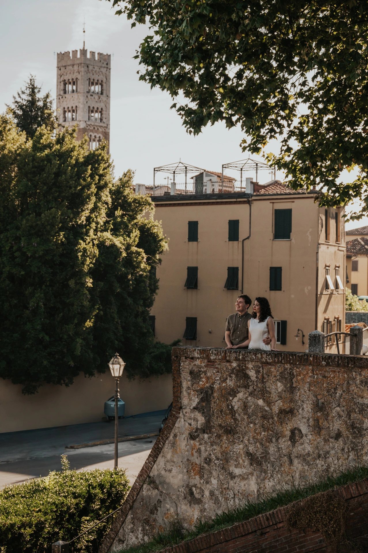 The couple beside a stone terrace with San Frediano’s bell tower rising above the nearby buildings during a couple photoshoot in Lucca.