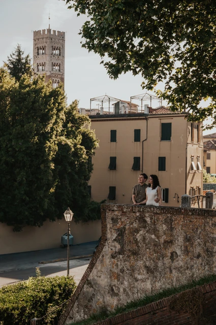 Lucca couple photoshoot: the stone terrace and San Frediano’s tower The couple beside a stone terrace with San Frediano’s bell tower rising above the nearby buildings during a couple photoshoot in Lucca.