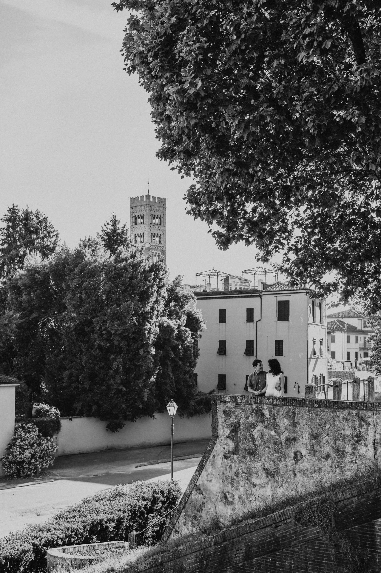 Black-and-white photograph of a view of the stone terrace, leafy trees and San Frediano’s bell tower during a couple photoshoot in Lucca.