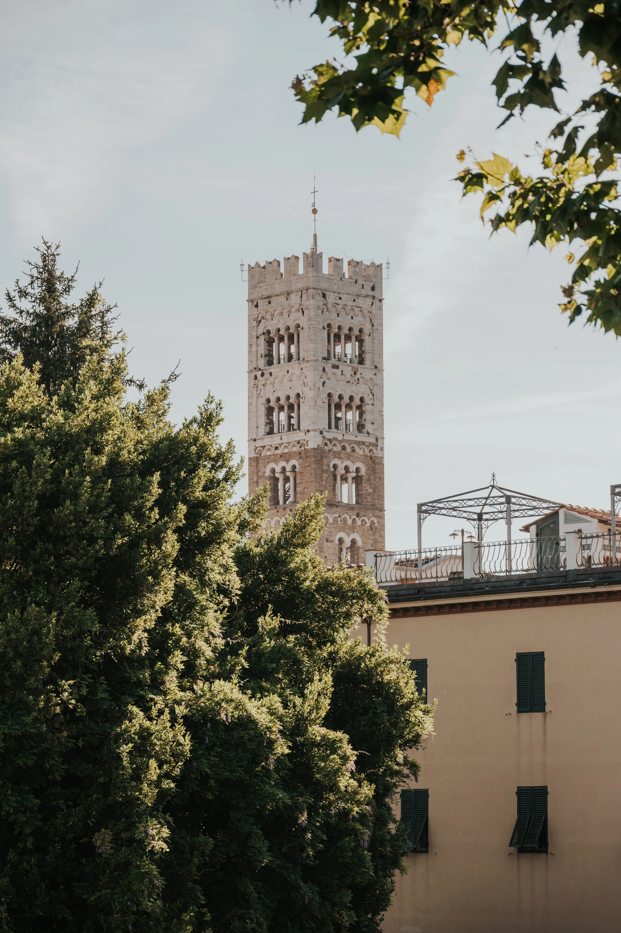 San Frediano’s stone bell tower rising above leafy trees and pale buildings during a couple photoshoot in Lucca.