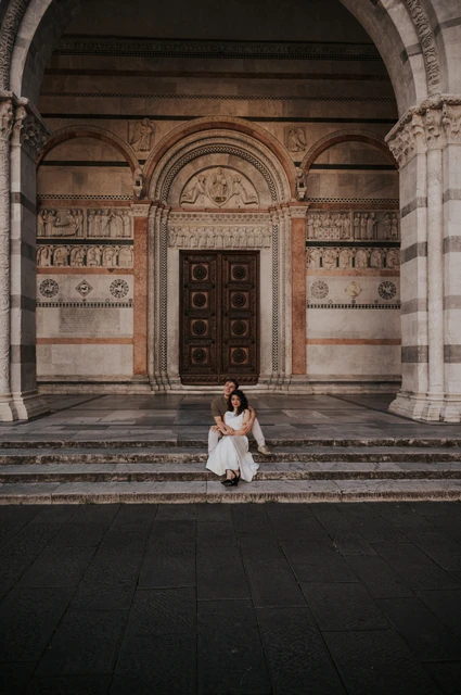 Lucca couple photoshoot: the Duomo’s arched porch and broad steps A wide view of the couple sitting on the steps beneath the Duomo di San Martino’s arched porch during a couple photoshoot in Lucca.