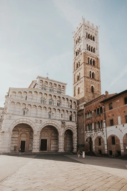 Lucca couple photoshoot: the Duomo façade and tall bell tower A wide view of the couple in the square beneath the Duomo di San Martino’s façade and tall bell tower during a couple photoshoot in Lucca.