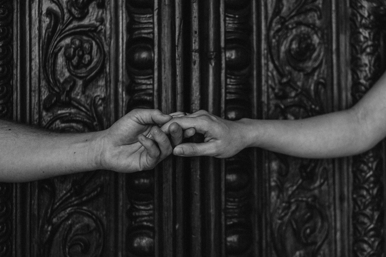 Lucca couple photoshoot: a detail of hands at the Duomo doorway in black and white Black-and-white photograph of a close detail of the couple’s hands meeting in front of the Duomo di San Martino’s wooden door panels during a couple photoshoot in Lucca.