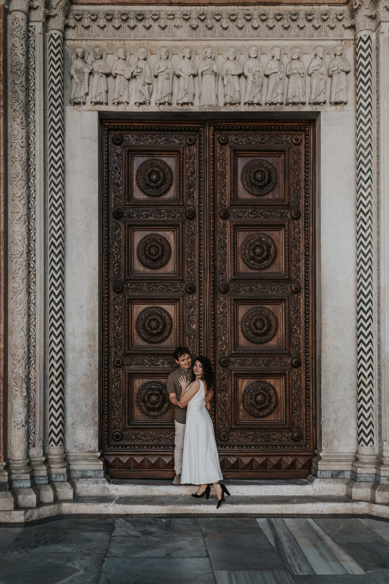 The couple standing close in front of the Duomo di San Martino’s large carved wooden doors during a couple photoshoot in Lucca.