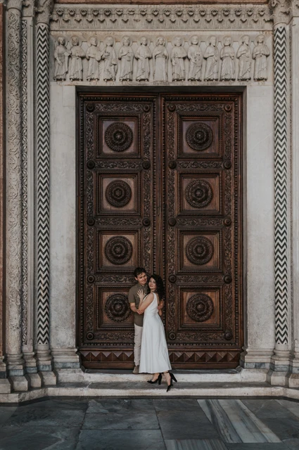Lucca couple photoshoot: a portrait at San Martino’s carved doors The couple standing close in front of the Duomo di San Martino’s large carved wooden doors during a couple photoshoot in Lucca.