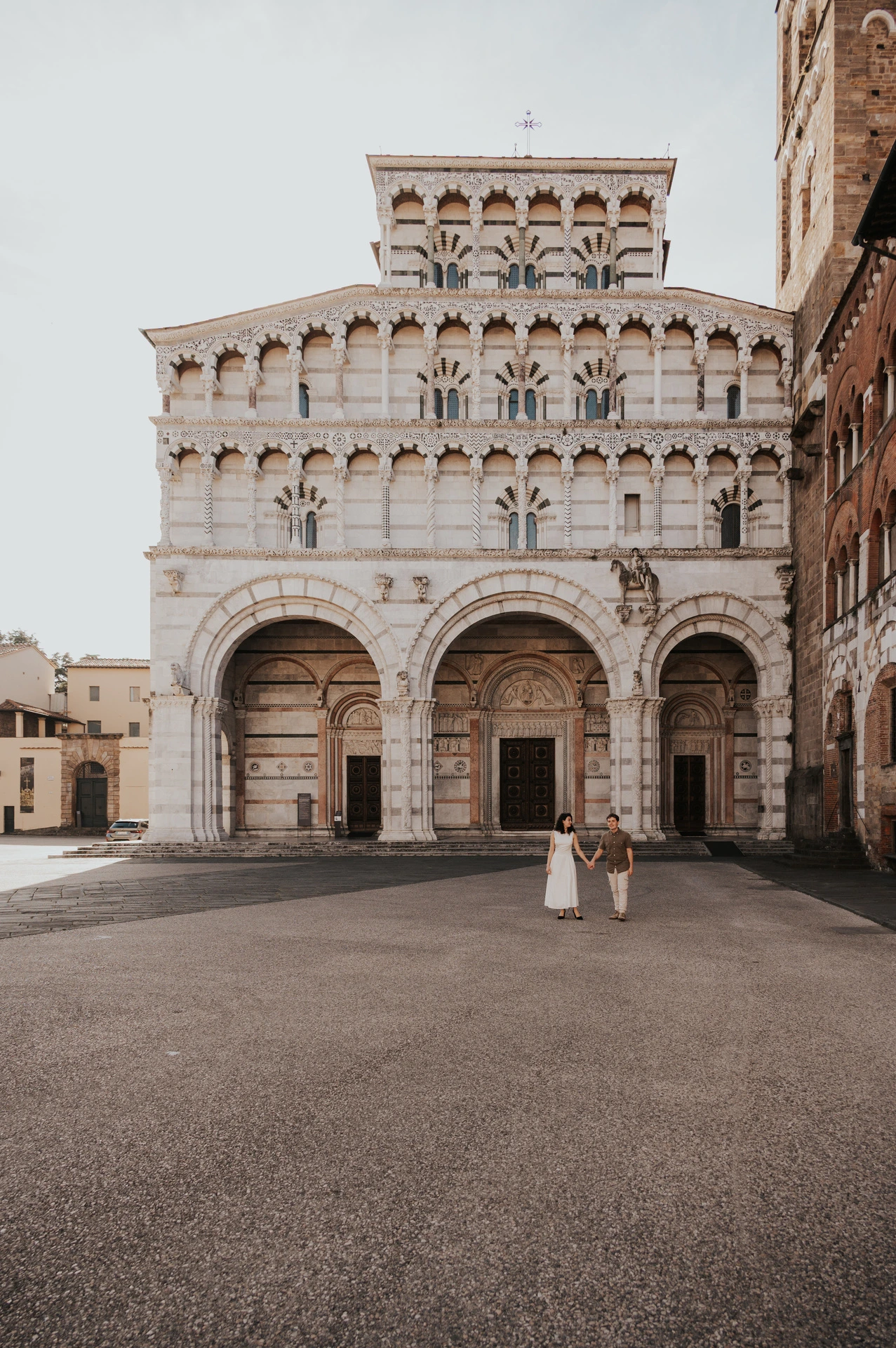 The couple standing in the square with the ornate façade of the Duomo di San Martino behind them during a couple photoshoot in Lucca.