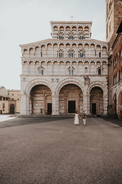 The couple standing in the square with the ornate façade of the Duomo di San Martino behind them during a couple photoshoot in Lucca.