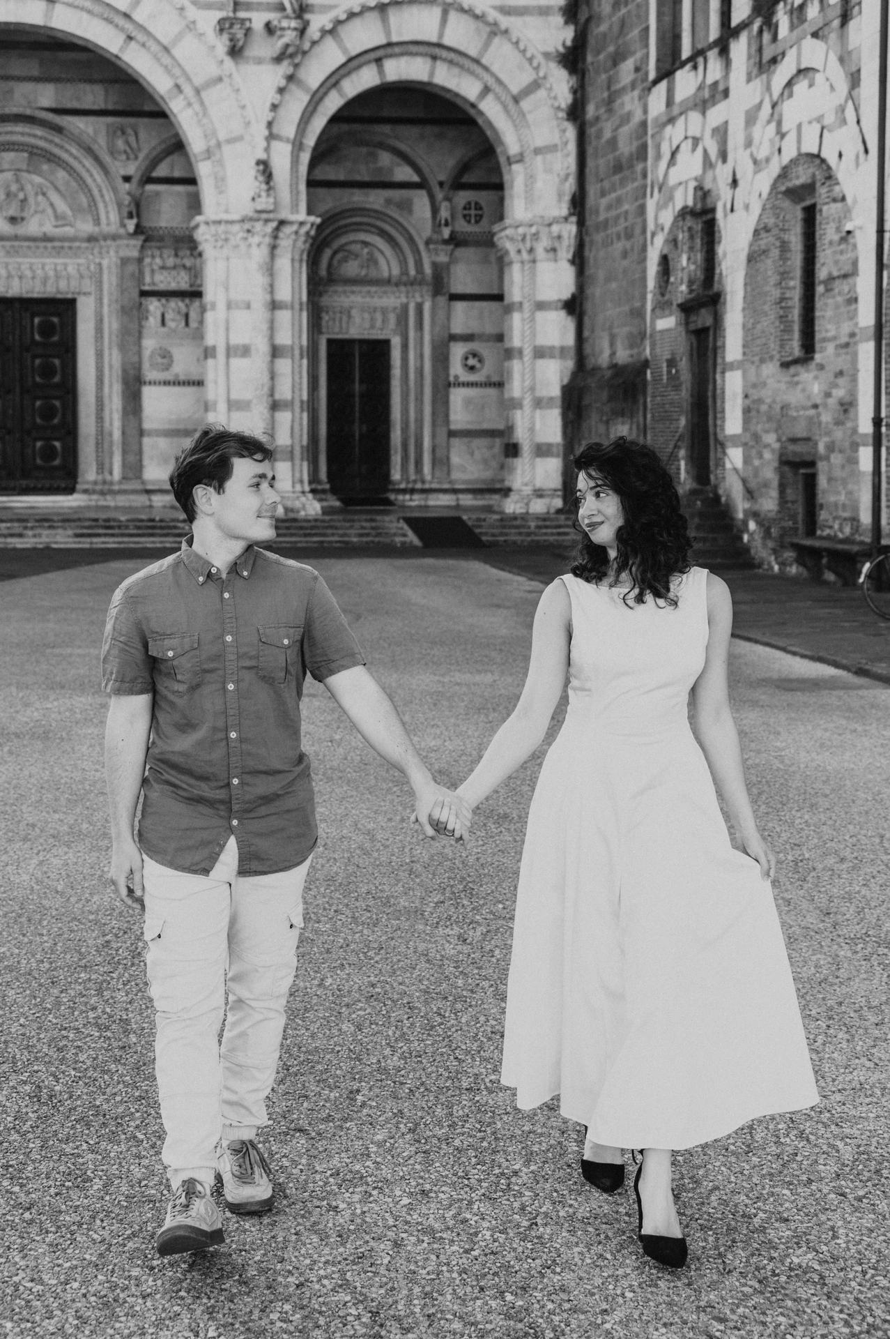 Black-and-white photograph of the couple walking hand in hand across the square outside the Duomo di San Martino during a couple photoshoot in Lucca.