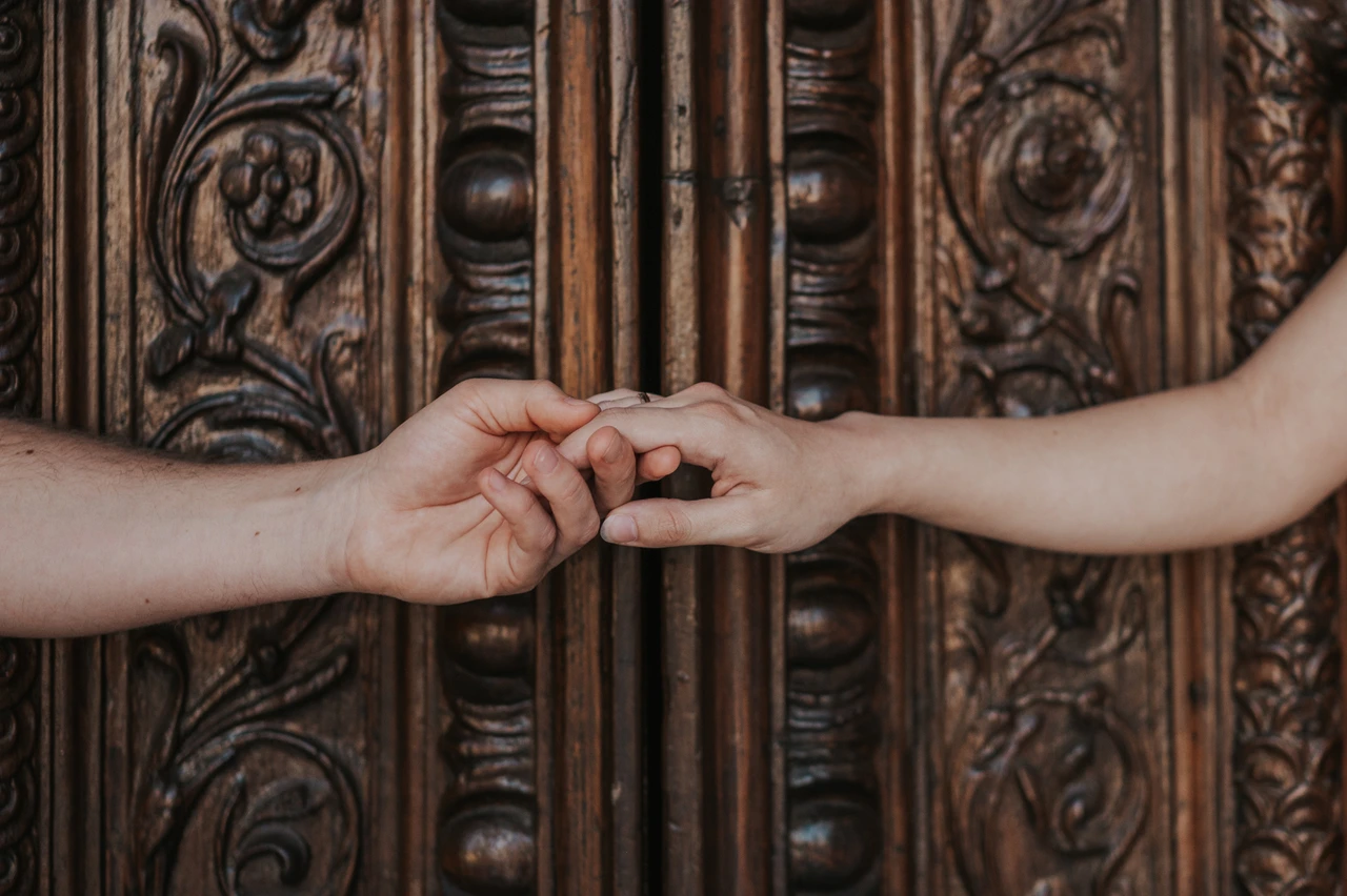 Lucca couple photoshoot: joined hands against carved wooden doors A close detail of the couple’s joined hands against the Duomo di San Martino’s carved wooden doors during a couple photoshoot in Lucca.