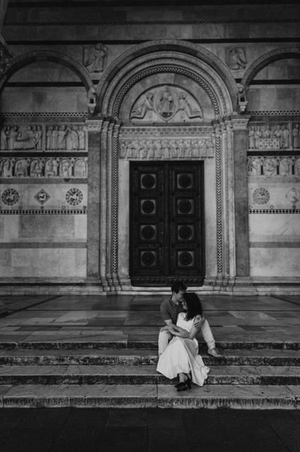 Lucca couple photoshoot: sitting beneath San Martino’s carved doorway in black and white Black-and-white photograph of the couple sitting close on the stone steps beneath the carved doorway of the Duomo di San Martino during a couple photoshoot in Lucca.