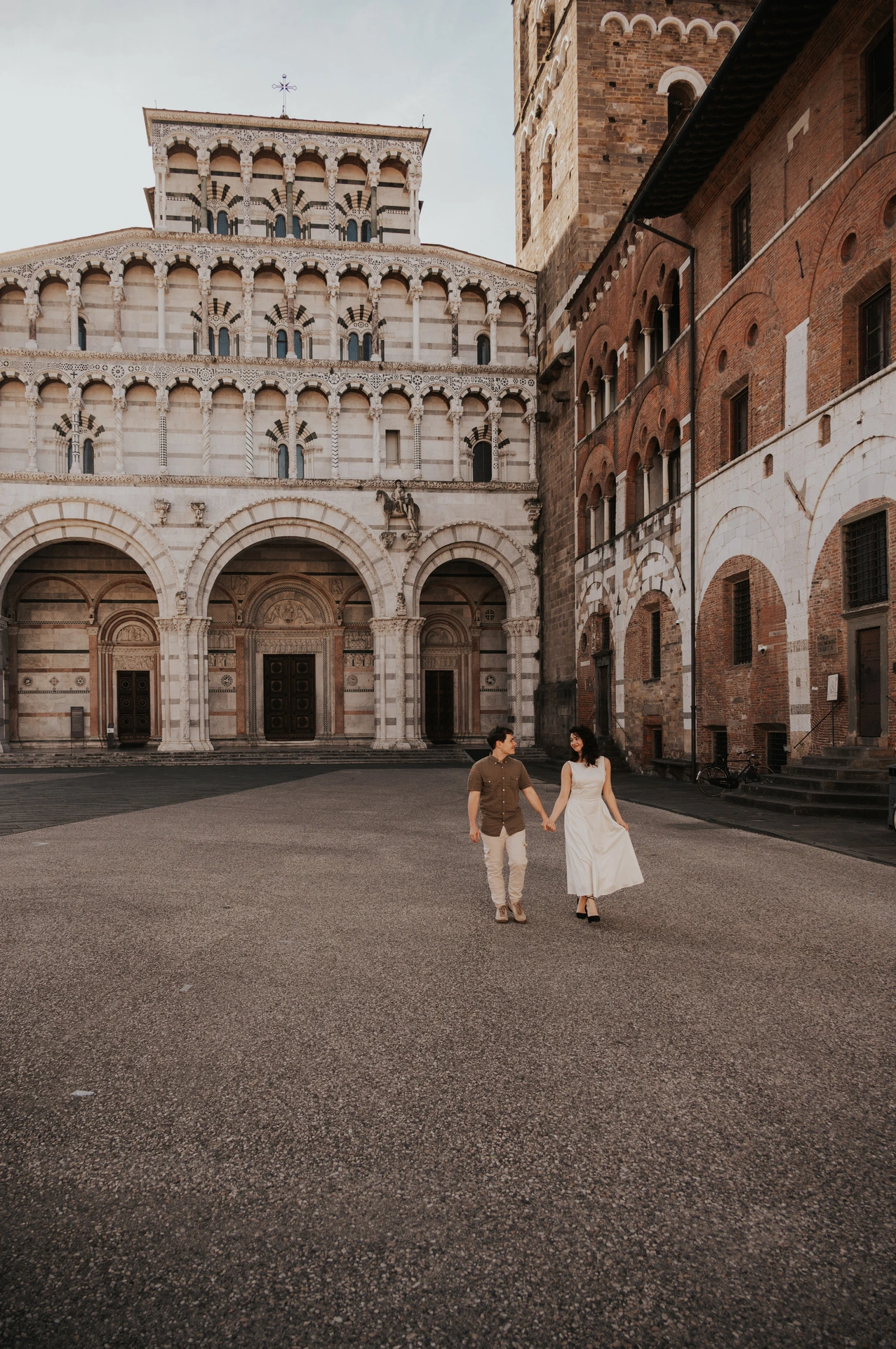 The couple walking together across the square with the Duomo di San Martino’s arches behind them during a couple photoshoot in Lucca.