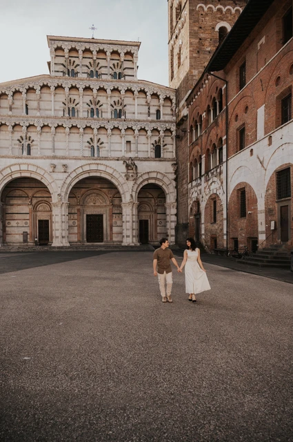 Lucca couple photoshoot: a walk across the square by San Martino The couple walking together across the square with the Duomo di San Martino’s arches behind them during a couple photoshoot in Lucca.