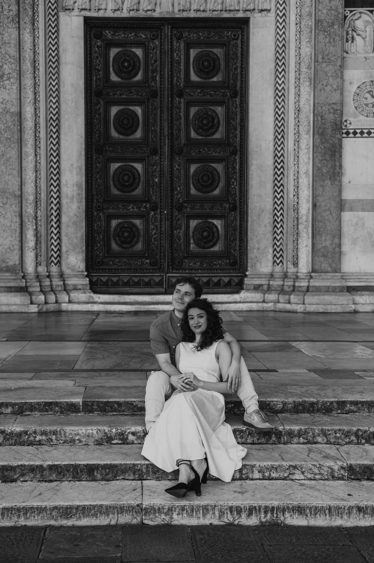 Black-and-white photograph of a close portrait of the couple sitting together beneath the Duomo di San Martino’s carved doorway during a couple photoshoot in Lucca.