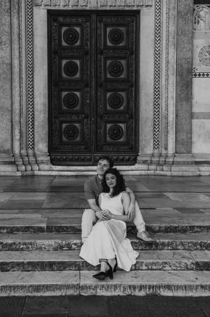 Lucca couple photoshoot: a close portrait beneath the Duomo doorway in black and white Black-and-white photograph of a close portrait of the couple sitting together beneath the Duomo di San Martino’s carved doorway during a couple photoshoot in Lucca.