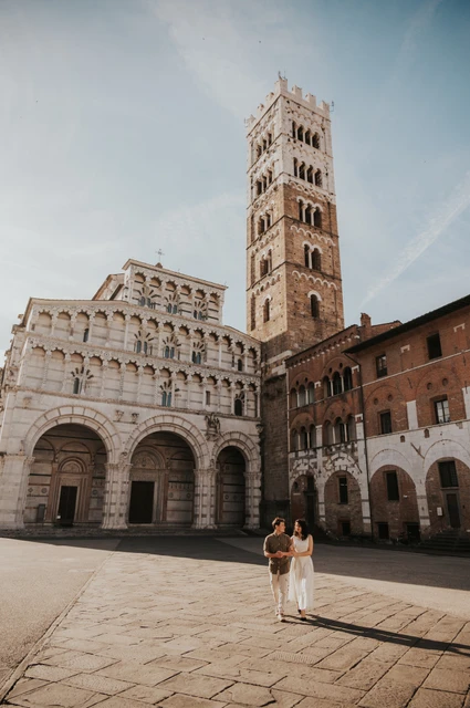 Lucca couple photoshoot: a walk with San Martino’s tower in view The couple walking together across the paving with the Duomo di San Martino and its bell tower behind them during a couple photoshoot in Lucca.