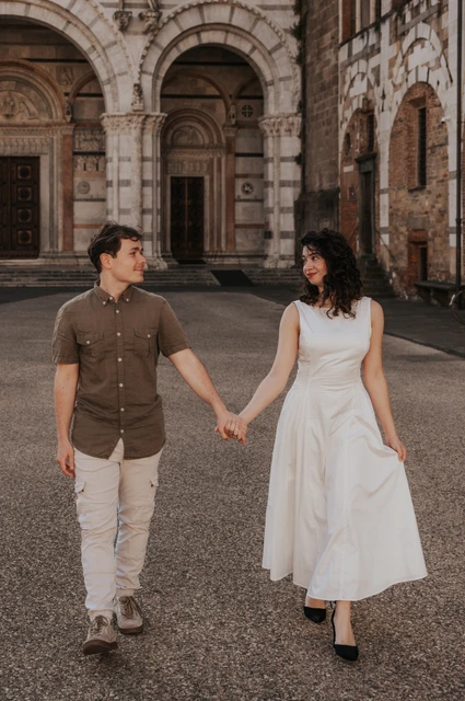 Lucca couple photoshoot: walking hand in hand outside San Martino The couple walking hand in hand towards the camera with the Duomo di San Martino behind them during a couple photoshoot in Lucca.