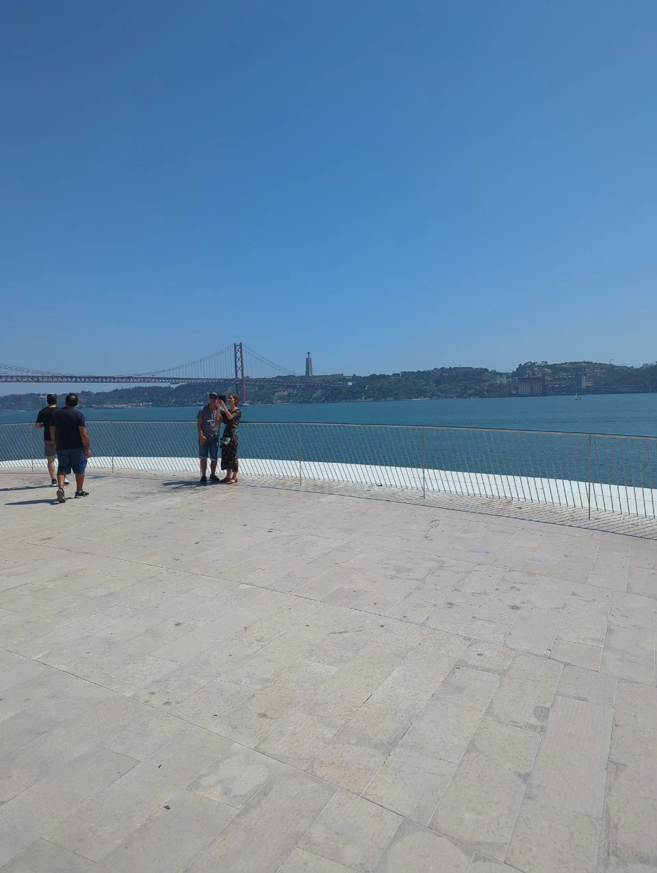 Visitors cross MAAT's pale rooftop promenade above the Tagus, with the 25 de Abril Bridge and Cristo Rei across the water.