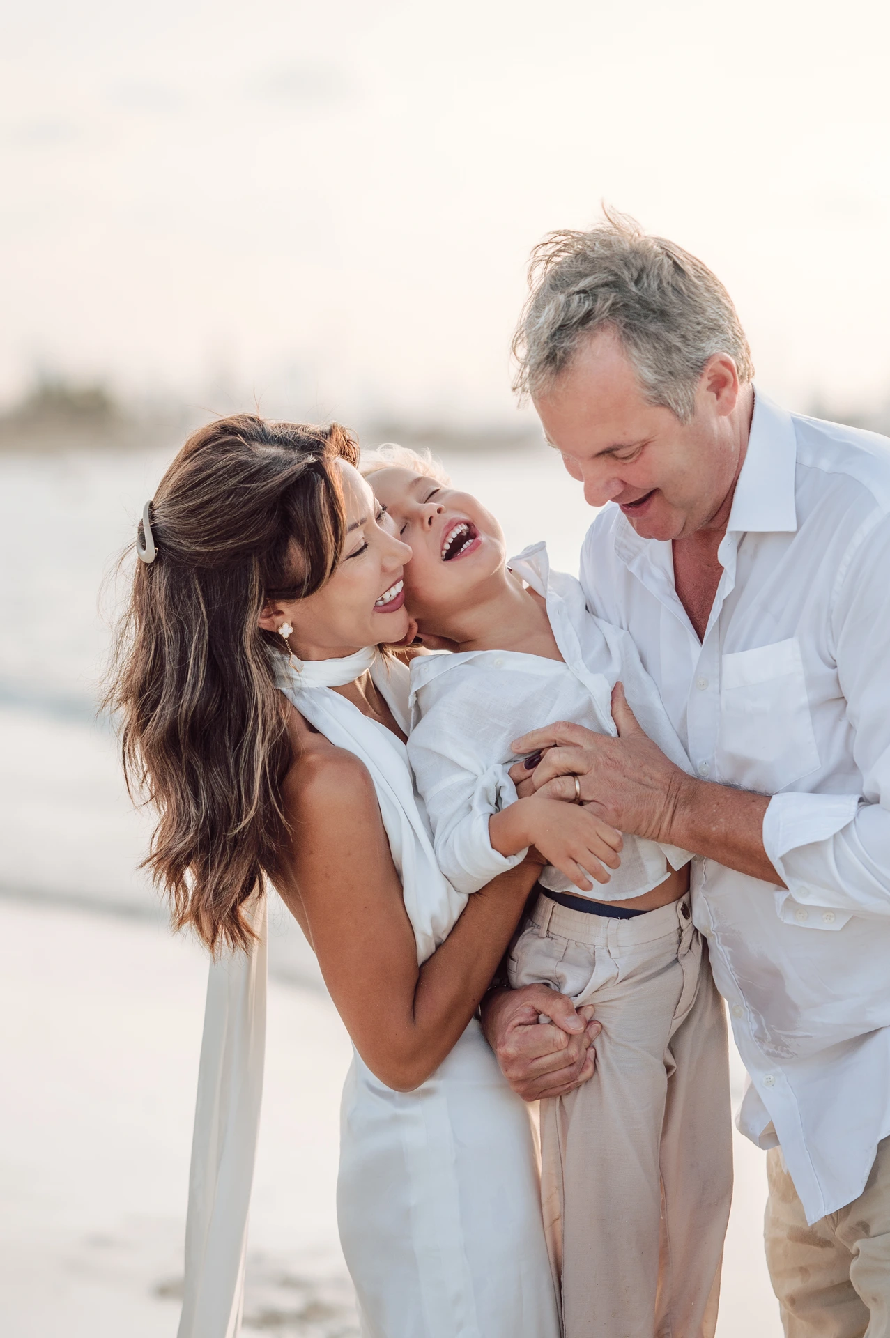Parents cuddle and laugh with their child on Dubai beach, captured as an intimate family beach photoshoot close-up.