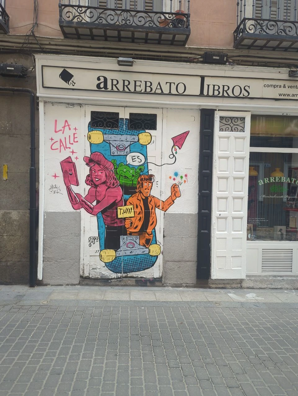 A brightly illustrated bookshop shutter adds bold colour and lettering to a cobbled Malasaña street in Madrid for a graphic photoshoot setting.