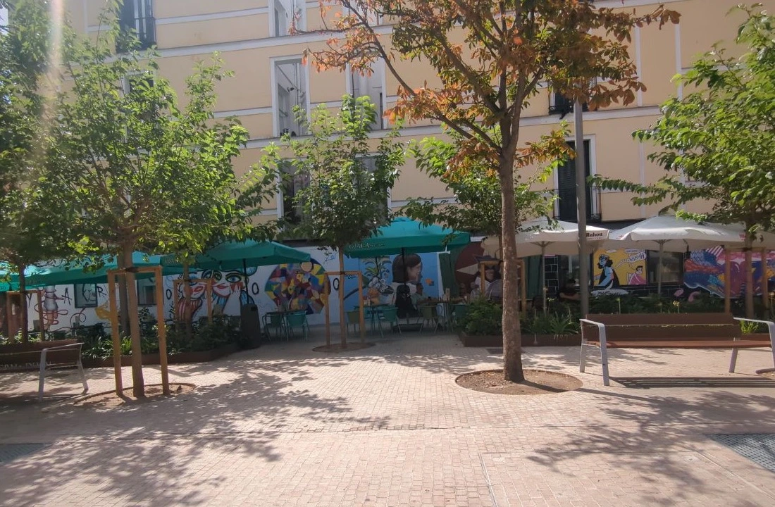 A sunny Malasaña square in Madrid offers leafy trees, café terraces and colourful graphic murals as a relaxed photoshoot backdrop.