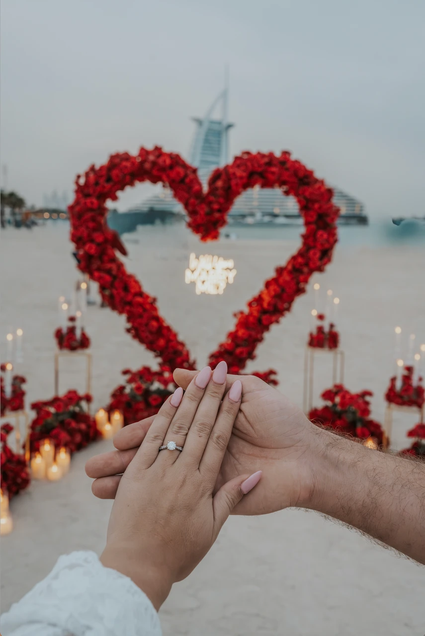 Heart Proposal Setup Dubai - ring close-up with Burj backdrop Hands are framed in front of a red heart proposal setup in Dubai, showing the engagement ring with Burj Al Arab softly blurred in the background.