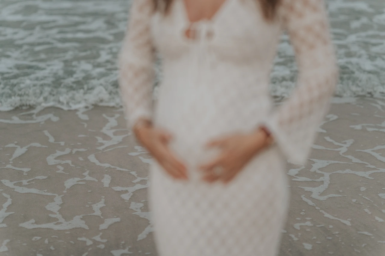 Beach maternity photoshoot Dubai - soft-focus white dress close-up Soft-focus close-up of a pregnant woman in a white dress on Dubai shoreline during a beach maternity photoshoot.